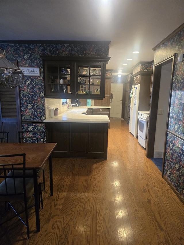 kitchen with hardwood / wood-style floors, kitchen peninsula, white appliances, dark brown cabinets, and sink