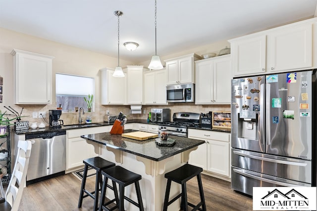 kitchen with white cabinets, appliances with stainless steel finishes, a center island, sink, and hanging light fixtures