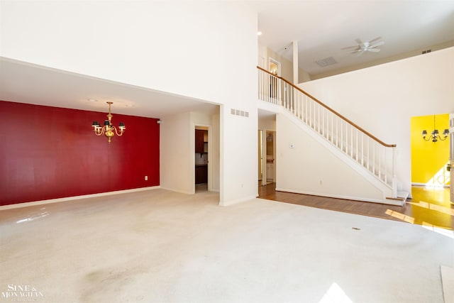 unfurnished living room with ceiling fan with notable chandelier, a high ceiling, and carpet floors