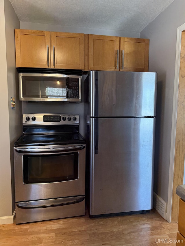 kitchen with appliances with stainless steel finishes and light hardwood / wood-style floors