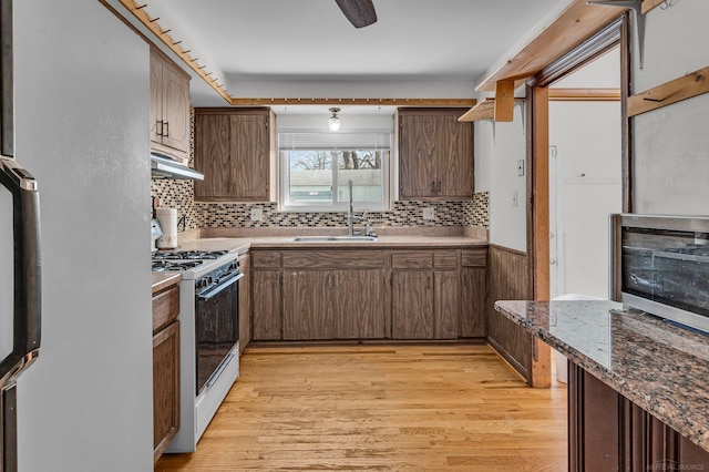 kitchen with light wood-type flooring, white gas stove, fridge, and sink