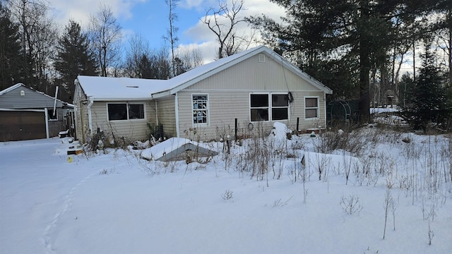 snow covered rear of property featuring a garage and an outbuilding