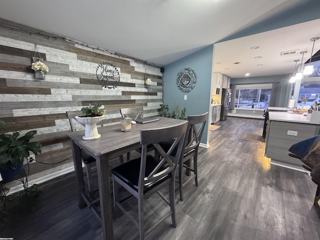 dining space with visible vents, dark wood-style flooring, wooden walls, baseboards, and an accent wall