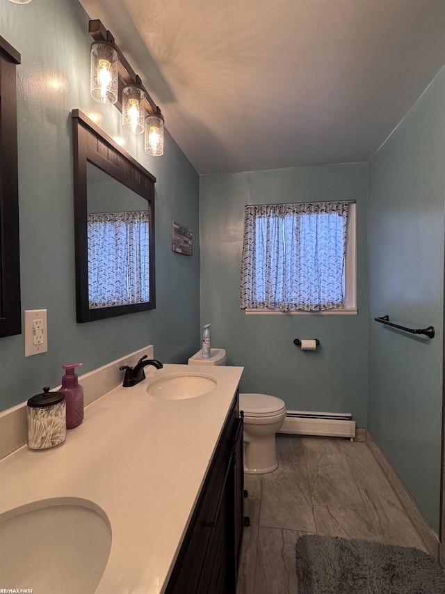 bathroom featuring double vanity, toilet, a baseboard heating unit, and a sink