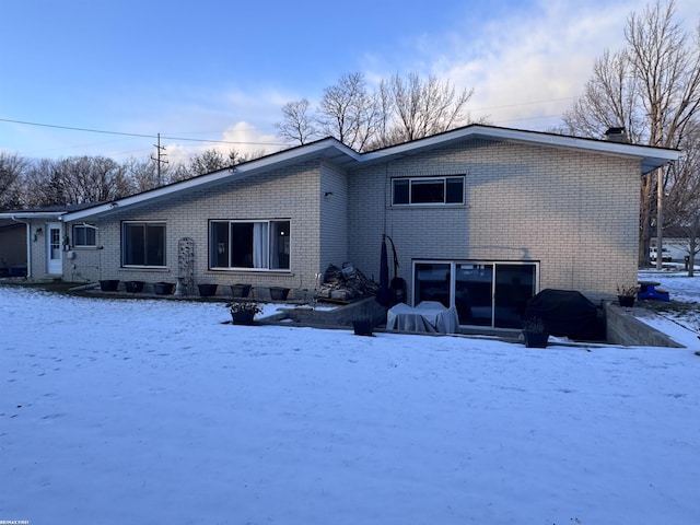 snow covered rear of property with brick siding