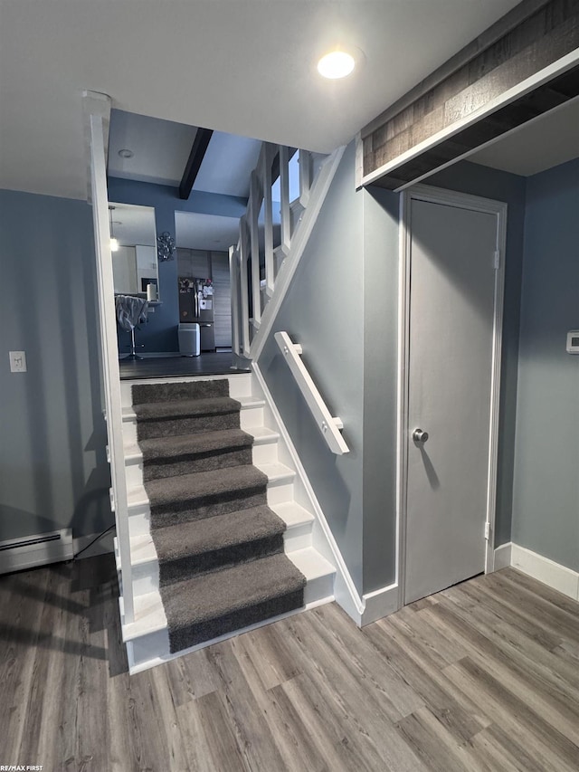 stairway featuring a baseboard heating unit, baseboards, and wood finished floors