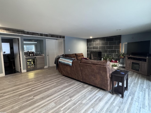 living area with wine cooler, an accent wall, a fireplace, and light wood finished floors