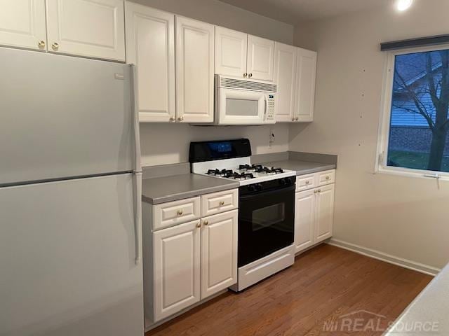 kitchen with dark wood-type flooring, white cabinets, refrigerator, and range with gas stovetop