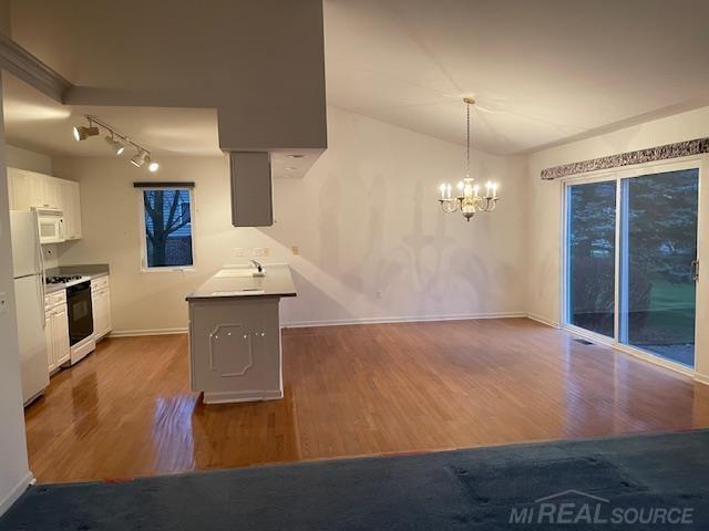 kitchen with pendant lighting, white appliances, white cabinets, kitchen peninsula, and hardwood / wood-style flooring