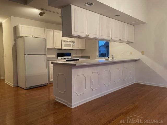 kitchen with white appliances, white cabinets, dark hardwood / wood-style floors, and kitchen peninsula