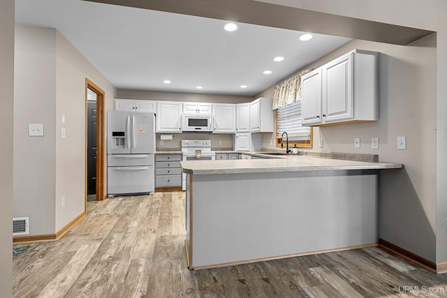 kitchen with kitchen peninsula, light hardwood / wood-style flooring, sink, white cabinetry, and white appliances