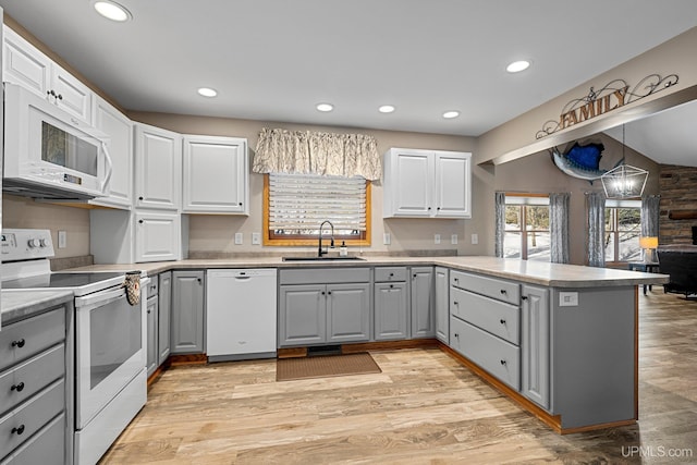 kitchen with kitchen peninsula, hanging light fixtures, sink, gray cabinets, and white appliances