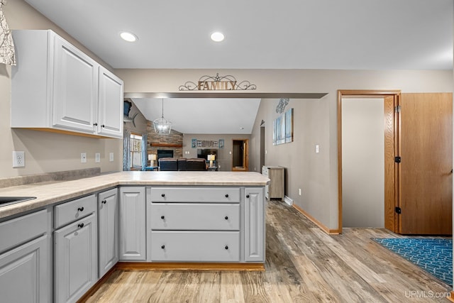 kitchen with light hardwood / wood-style floors, white cabinetry, kitchen peninsula, pendant lighting, and lofted ceiling