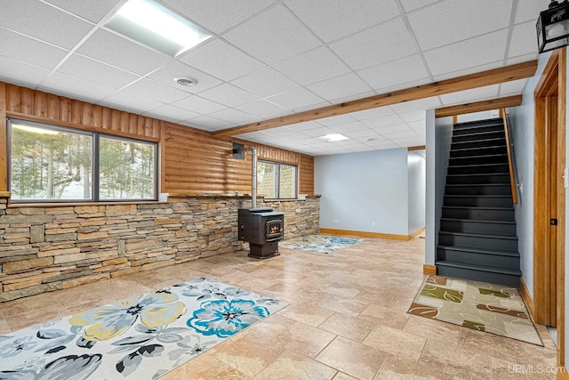 basement with a wood stove, wooden walls, plenty of natural light, and a drop ceiling