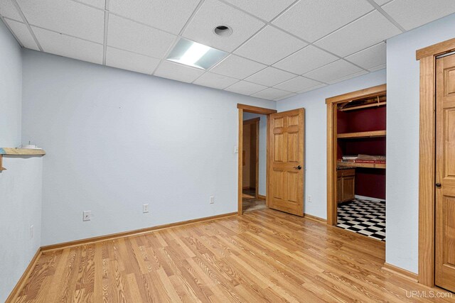 unfurnished bedroom with a paneled ceiling, a closet, and light hardwood / wood-style flooring