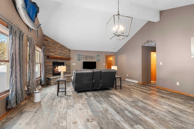 living room featuring a stone fireplace, hardwood / wood-style floors, an inviting chandelier, and lofted ceiling