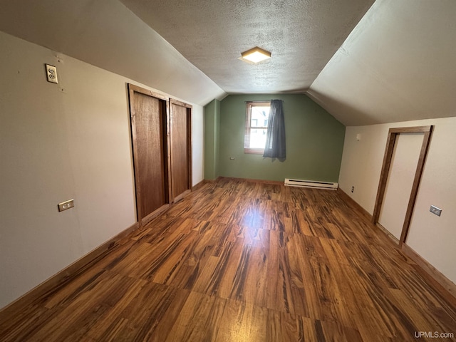 additional living space featuring dark wood-type flooring, a textured ceiling, a baseboard heating unit, and lofted ceiling