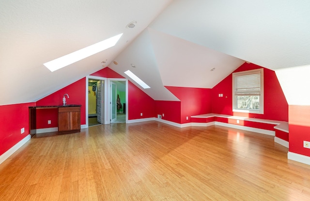 additional living space with sink, lofted ceiling with skylight, and hardwood / wood-style floors