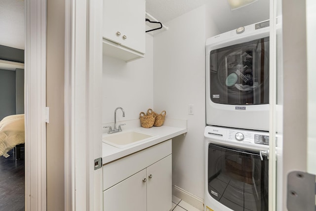 laundry area featuring a textured ceiling, cabinets, stacked washer and dryer, sink, and light tile patterned flooring