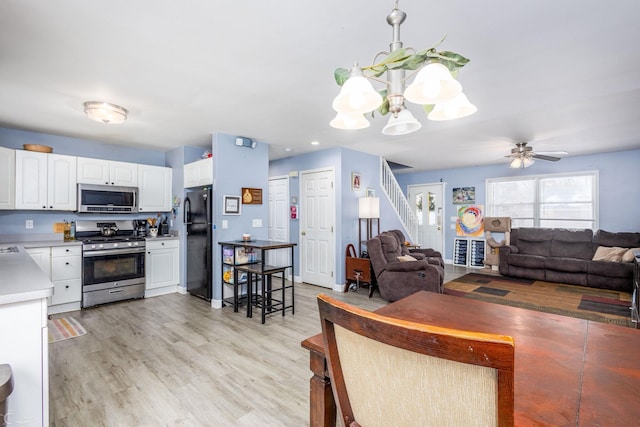 kitchen with white cabinets, light wood-type flooring, sink, stainless steel appliances, and ceiling fan with notable chandelier