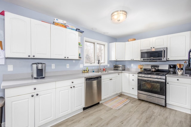 kitchen with sink, white cabinets, light wood-type flooring, and appliances with stainless steel finishes