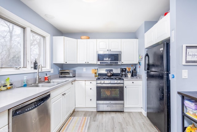 kitchen with white cabinets, appliances with stainless steel finishes, light hardwood / wood-style flooring, and sink