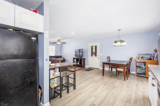 kitchen with decorative light fixtures, light hardwood / wood-style floors, black fridge, and white cabinetry