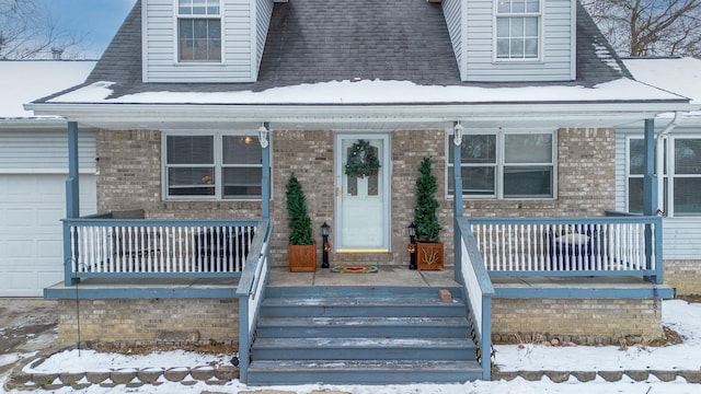 snow covered property entrance featuring a porch and a garage