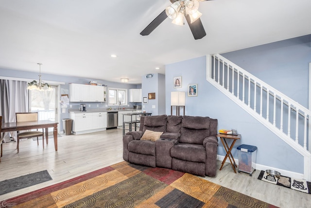 living room with light wood-type flooring and ceiling fan with notable chandelier