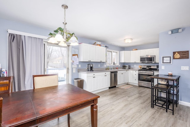 kitchen featuring white cabinets, stainless steel appliances, hanging light fixtures, a notable chandelier, and light wood-type flooring