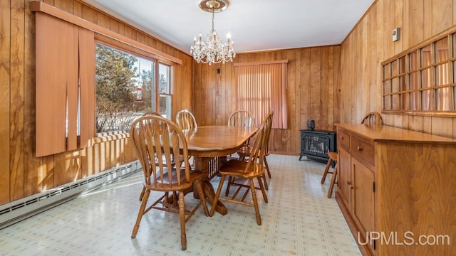 dining room with a wood stove, a chandelier, wooden walls, and a baseboard heating unit