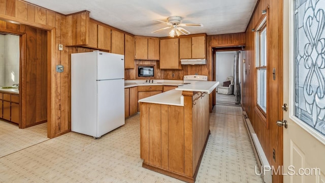 kitchen with ceiling fan, sink, white appliances, a center island, and wooden walls