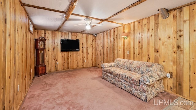 living area featuring ceiling fan, wood walls, beamed ceiling, and carpet