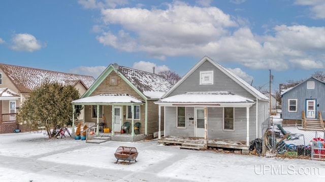 snow covered back of property featuring covered porch and a fire pit