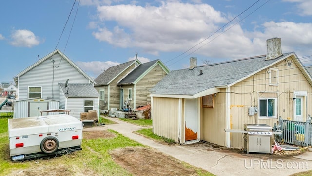 back of house featuring a storage unit, an outdoor structure, and a shingled roof