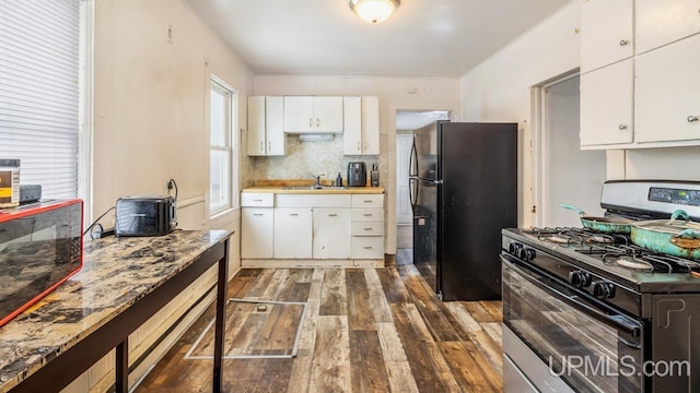 kitchen with white cabinetry, gas range, black fridge, backsplash, and dark hardwood / wood-style floors