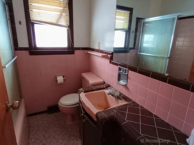 bathroom featuring a healthy amount of sunlight, toilet, vanity, and tile walls