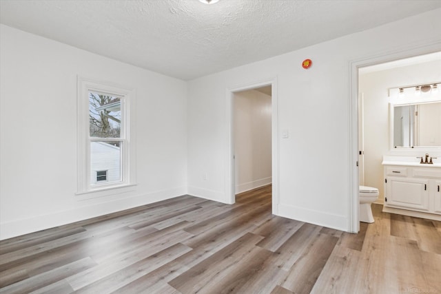 spare room featuring sink, light wood-type flooring, and a textured ceiling