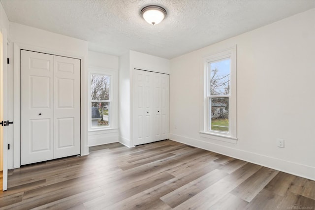 unfurnished bedroom with multiple closets, light wood-type flooring, and a textured ceiling