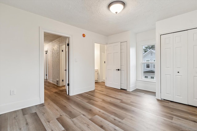 unfurnished bedroom with a textured ceiling, light hardwood / wood-style flooring, and two closets