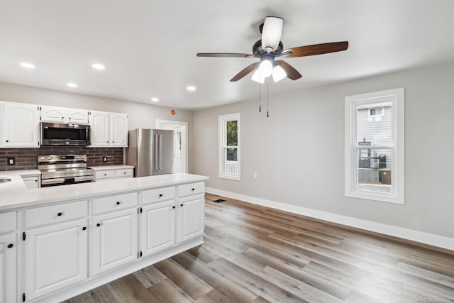 kitchen featuring white cabinets, stainless steel appliances, tasteful backsplash, ceiling fan, and light hardwood / wood-style flooring