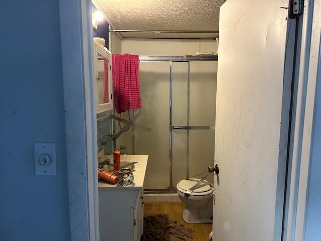 bathroom with a textured ceiling, vanity, hardwood / wood-style flooring, toilet, and a shower with shower door