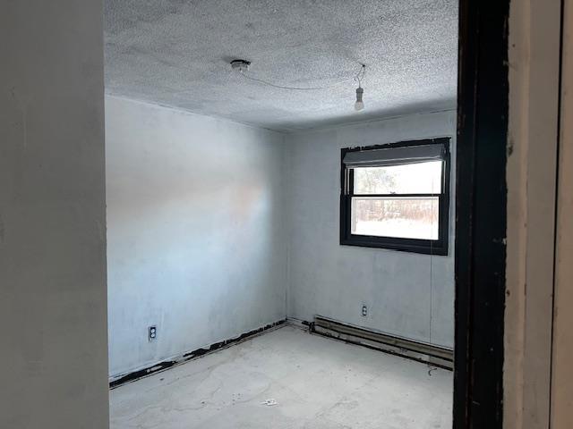 empty room with a textured ceiling and a baseboard heating unit