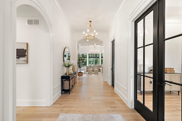 hallway featuring light wood-type flooring, french doors, a chandelier, and ornamental molding