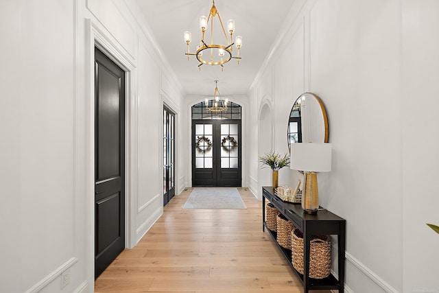 entrance foyer with crown molding, an inviting chandelier, light hardwood / wood-style floors, and french doors