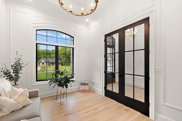 entryway with a notable chandelier, light wood-type flooring, french doors, and ornamental molding