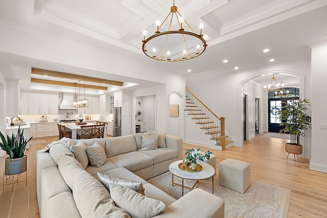 living room with coffered ceiling, an inviting chandelier, light wood-type flooring, and ornamental molding