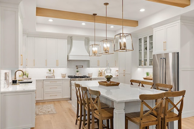 kitchen with pendant lighting, white cabinets, a kitchen island, sink, and custom range hood