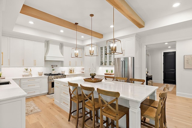 kitchen featuring a kitchen island, high end appliances, white cabinetry, and custom range hood