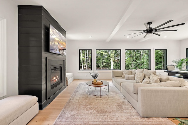 living room with ceiling fan, a large fireplace, beamed ceiling, and light wood-type flooring